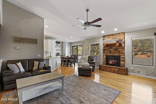 living room featuring lofted ceiling, a fireplace, ceiling fan, and light wood-type flooring