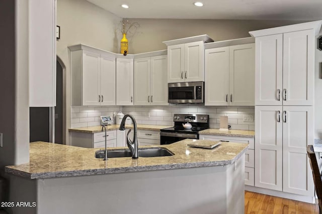 kitchen with lofted ceiling, sink, white cabinetry, stainless steel appliances, and light stone countertops