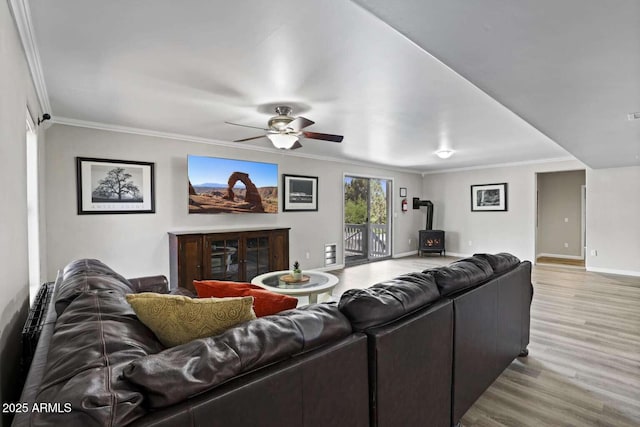 living room with crown molding, light wood-type flooring, ceiling fan, and a wood stove