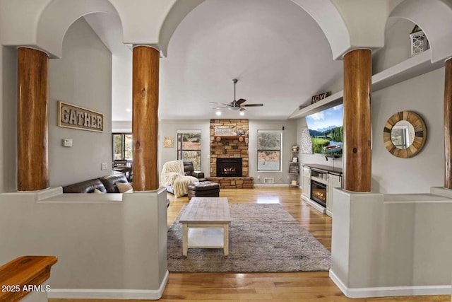 living room featuring a stone fireplace, decorative columns, light hardwood / wood-style floors, and ceiling fan