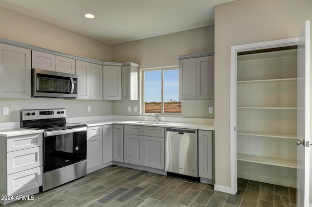 kitchen with dark wood-type flooring, appliances with stainless steel finishes, sink, and gray cabinetry