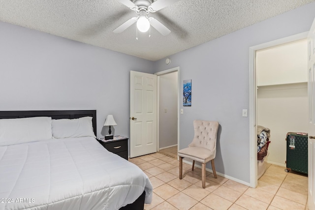 bedroom with ceiling fan, a walk in closet, a textured ceiling, and light tile patterned floors