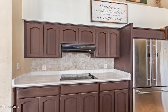 kitchen featuring black electric stovetop, tile counters, decorative backsplash, high end refrigerator, and dark brown cabinets