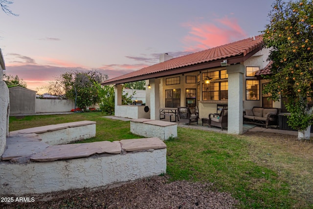 back house at dusk with a patio area, an outdoor living space, and a lawn