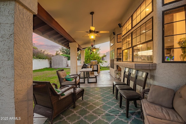 patio terrace at dusk with ceiling fan, an outdoor living space, and a shed