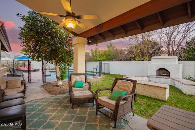 patio terrace at dusk with a fenced in pool, an outdoor stone fireplace, and ceiling fan