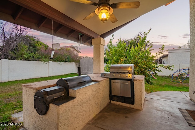 patio terrace at dusk with ceiling fan, a shed, exterior kitchen, and area for grilling