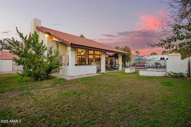 back house at dusk featuring a fenced in pool, a yard, and a patio