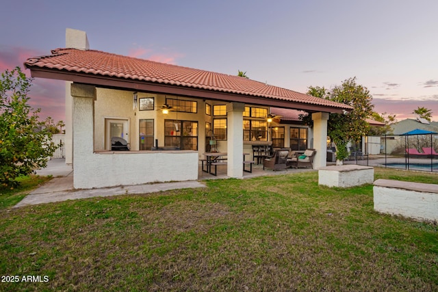 back house at dusk featuring a fenced in pool, a lawn, and a patio