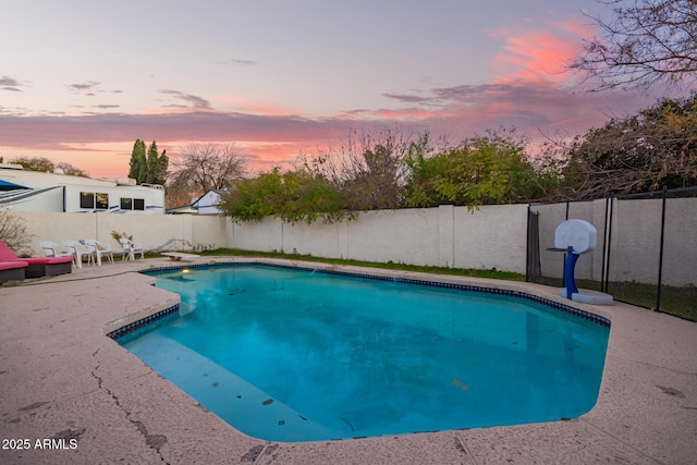 pool at dusk featuring a diving board and a patio area