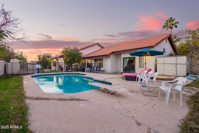 pool at dusk with a diving board and a patio