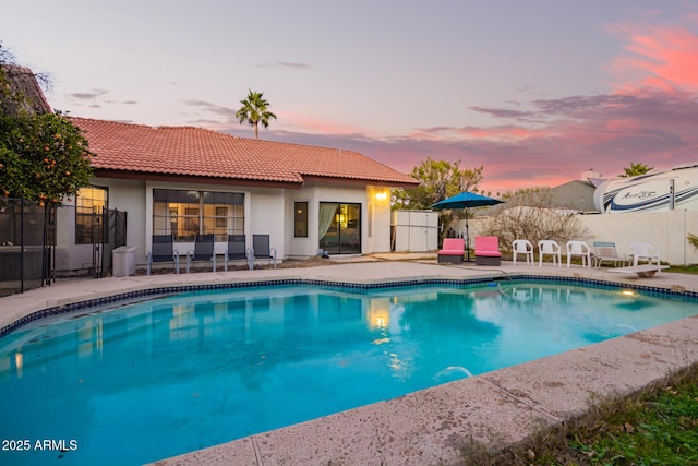 pool at dusk featuring a patio area and a diving board