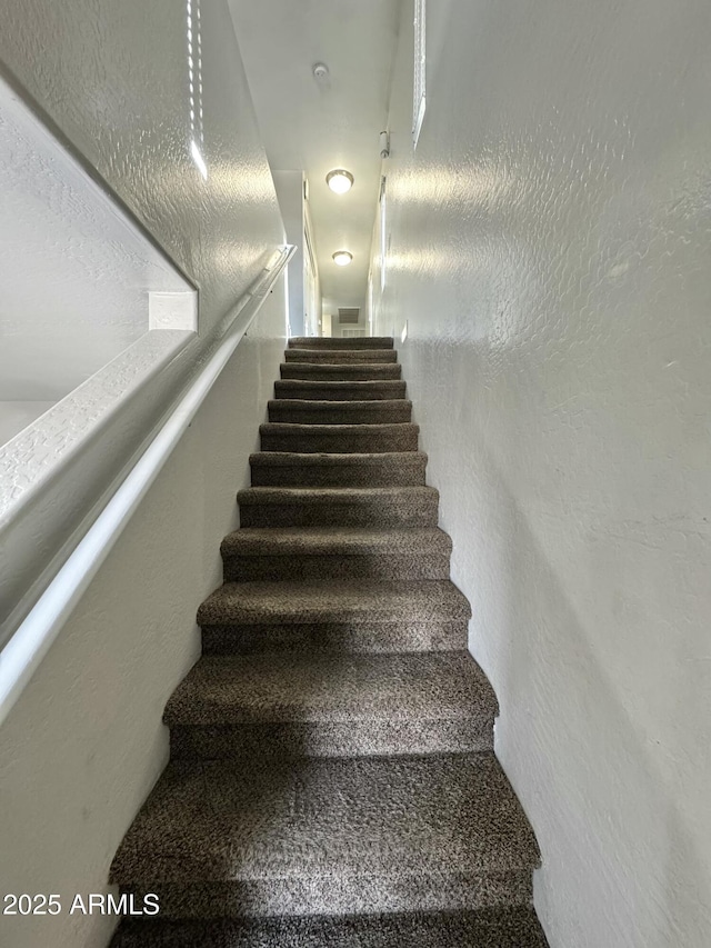 stairway featuring visible vents and a textured wall