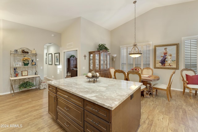 kitchen featuring light stone counters, light hardwood / wood-style flooring, high vaulted ceiling, pendant lighting, and a kitchen island