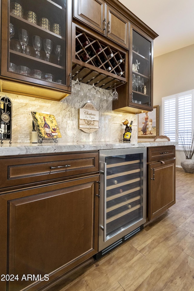 bar featuring backsplash, wine cooler, light stone counters, and dark brown cabinets