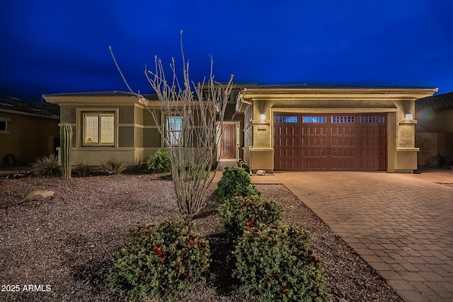 view of front of house with decorative driveway, an attached garage, and stucco siding