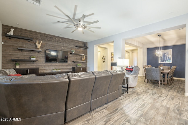 living area featuring an accent wall, ceiling fan with notable chandelier, visible vents, and wood walls