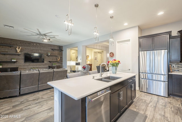 kitchen featuring visible vents, a sink, stainless steel appliances, light countertops, and wood walls