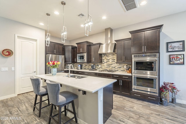 kitchen featuring a sink, visible vents, appliances with stainless steel finishes, and wall chimney exhaust hood