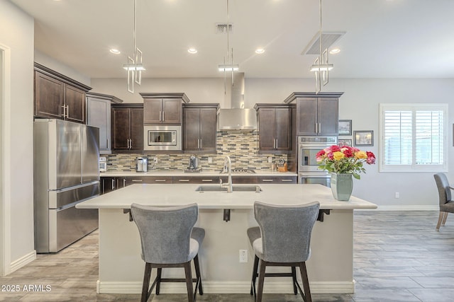 kitchen featuring visible vents, wall chimney range hood, dark brown cabinetry, stainless steel appliances, and a sink