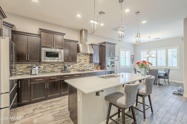 kitchen featuring backsplash, stainless steel appliances, wall chimney exhaust hood, and light countertops