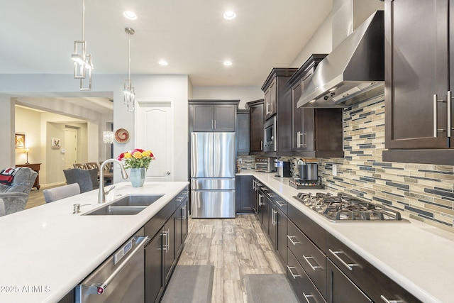 kitchen with a sink, stainless steel appliances, light countertops, dark brown cabinetry, and wall chimney exhaust hood