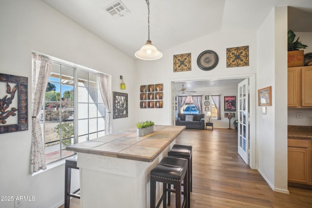 kitchen with ceiling fan, decorative light fixtures, dark hardwood / wood-style floors, a breakfast bar, and lofted ceiling