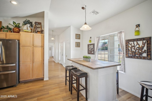 kitchen featuring a kitchen breakfast bar, light hardwood / wood-style flooring, light brown cabinetry, hanging light fixtures, and stainless steel refrigerator