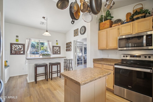 kitchen with appliances with stainless steel finishes, a kitchen island, decorative light fixtures, light brown cabinets, and light hardwood / wood-style flooring