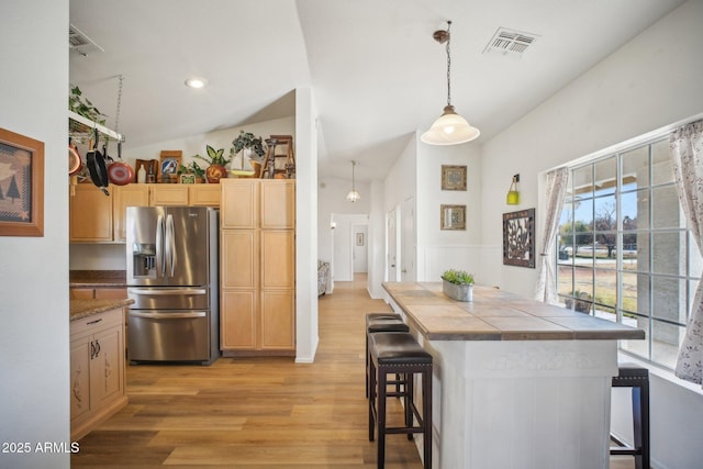 kitchen featuring decorative light fixtures, light brown cabinetry, stainless steel fridge with ice dispenser, light wood-type flooring, and a breakfast bar