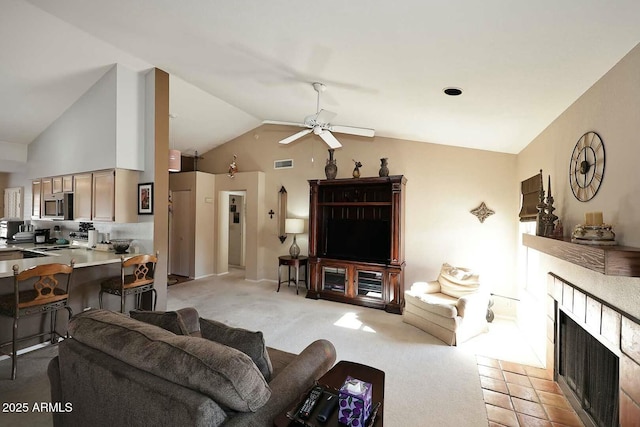 living room featuring light carpet, a tile fireplace, vaulted ceiling, and ceiling fan