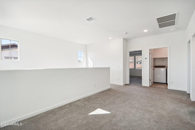 spare room featuring washer / clothes dryer, light colored carpet, and a healthy amount of sunlight