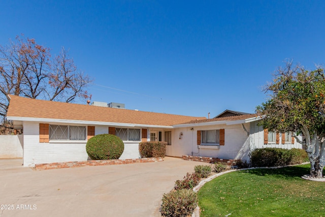 ranch-style house with brick siding, concrete driveway, a front yard, and roof with shingles