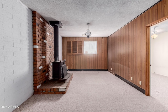 unfurnished living room with light colored carpet, a textured ceiling, a wood stove, and wood walls