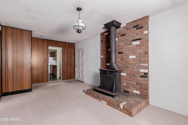 unfurnished living room with a textured ceiling, wood walls, a wood stove, and carpet