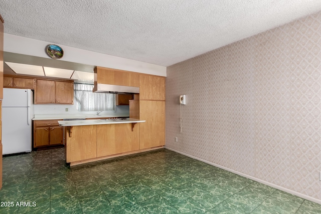 kitchen with wallpapered walls, dark floors, light countertops, a peninsula, and freestanding refrigerator