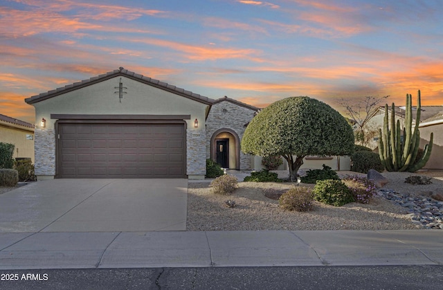 view of front of home featuring an attached garage, stone siding, a tiled roof, driveway, and stucco siding