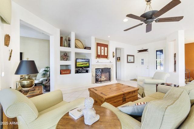 living room featuring built in shelves, light tile patterned flooring, recessed lighting, a ceiling fan, and a lit fireplace