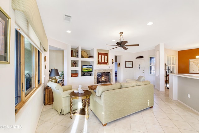 living room with a warm lit fireplace, light tile patterned floors, visible vents, built in features, and recessed lighting