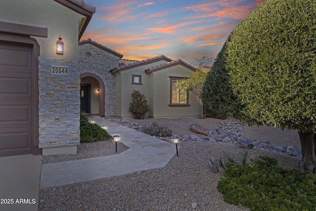 exterior space with a garage, stone siding, a tiled roof, and stucco siding