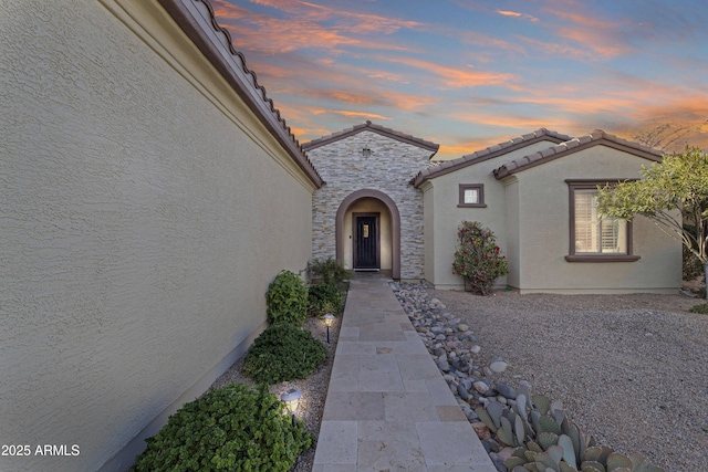 exterior entry at dusk featuring stone siding, a tiled roof, and stucco siding