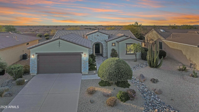 mediterranean / spanish home featuring a tile roof, stucco siding, an attached garage, stone siding, and driveway