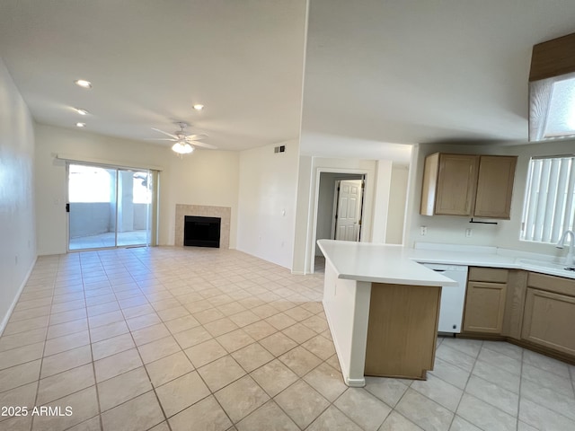 kitchen with light tile patterned floors, a tiled fireplace, dishwasher, ceiling fan, and light countertops