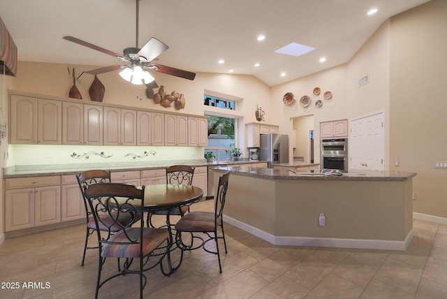 kitchen with a skylight, ceiling fan, stainless steel appliances, dark stone countertops, and a kitchen island