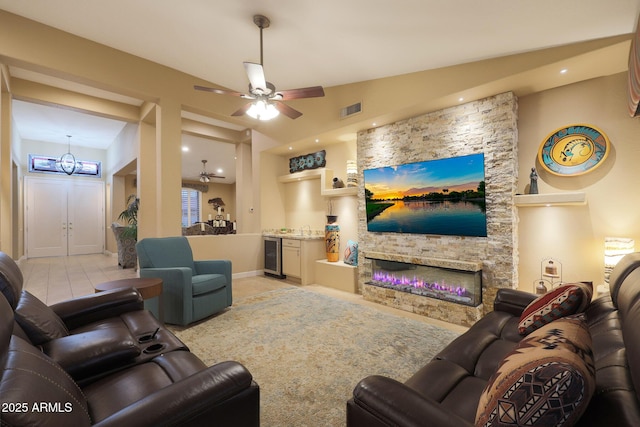 tiled living room featuring wine cooler, ceiling fan, a stone fireplace, and lofted ceiling