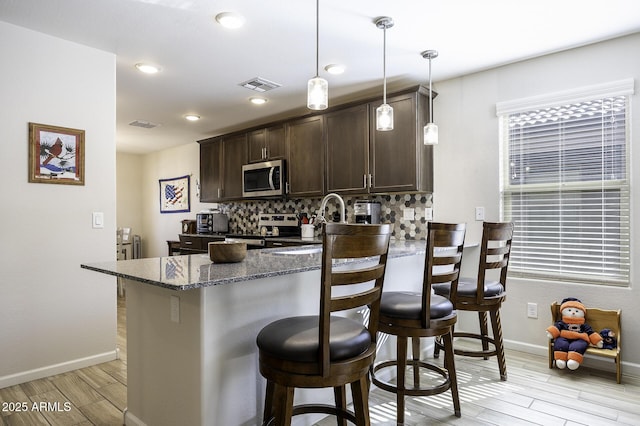 kitchen featuring pendant lighting, backsplash, a kitchen bar, dark stone counters, and stainless steel appliances