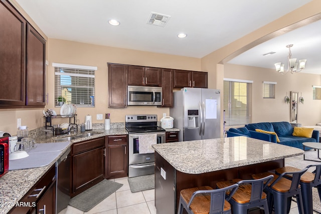 kitchen with a center island, a notable chandelier, a kitchen breakfast bar, pendant lighting, and appliances with stainless steel finishes