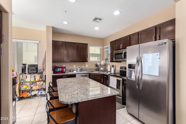 kitchen featuring stainless steel appliances, light tile patterned floors, a kitchen breakfast bar, a kitchen island, and dark brown cabinets