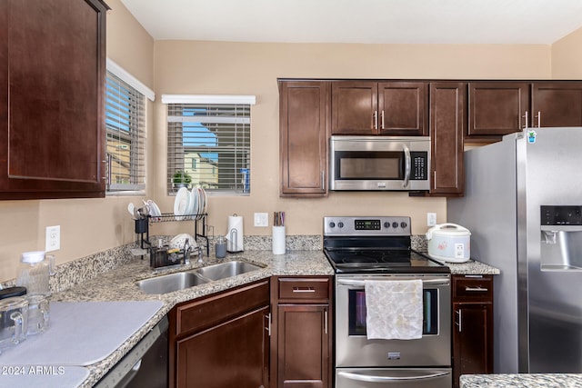 kitchen featuring dark brown cabinets, appliances with stainless steel finishes, sink, and light stone countertops