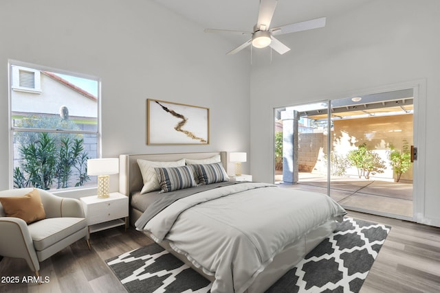 bedroom with access to exterior, wood-type flooring, ceiling fan, and a high ceiling